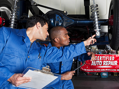 Two mechanics examining the shocks of a vehicle on a car lift.