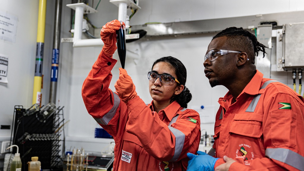 Woman and man looking at a tube wearing ExxonMobil Guyana safety uniforms
