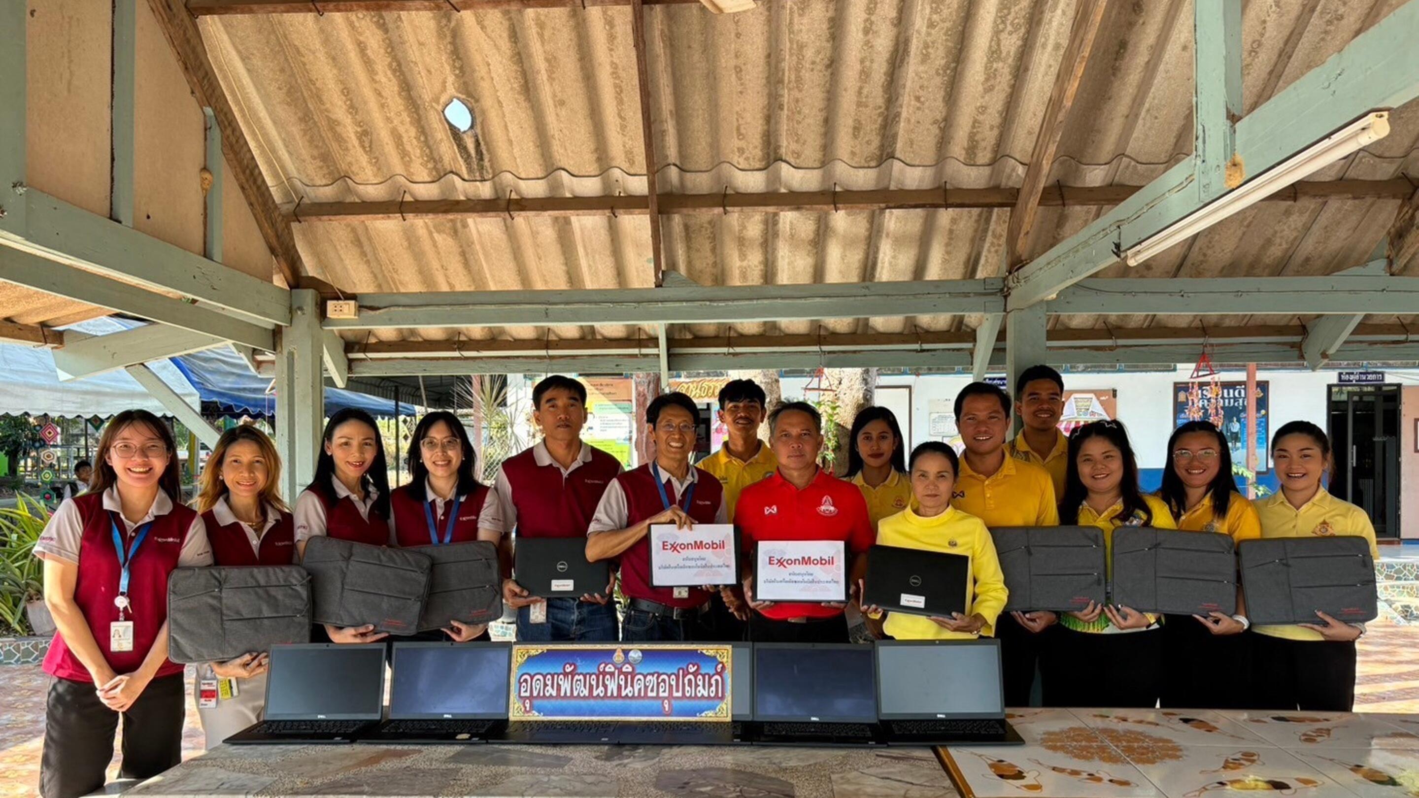 group photo of ExxonMobil affiliate staff representatives and school recipients holding laptops donated