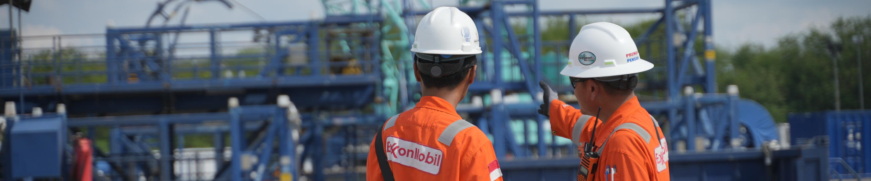 Employees in Indonesia in hard hats pointing and looking at equipment