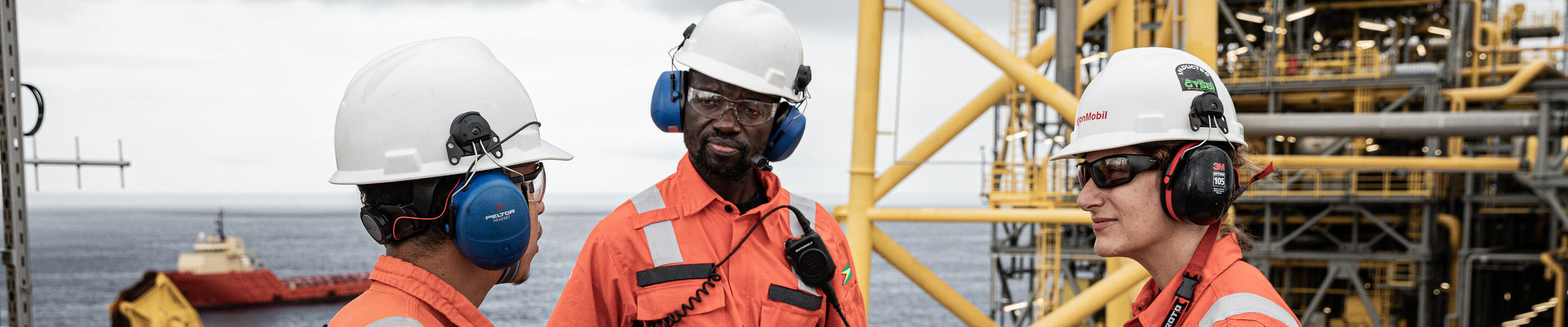 Three employees in hard hats talking on a vessel with the ocean in the background