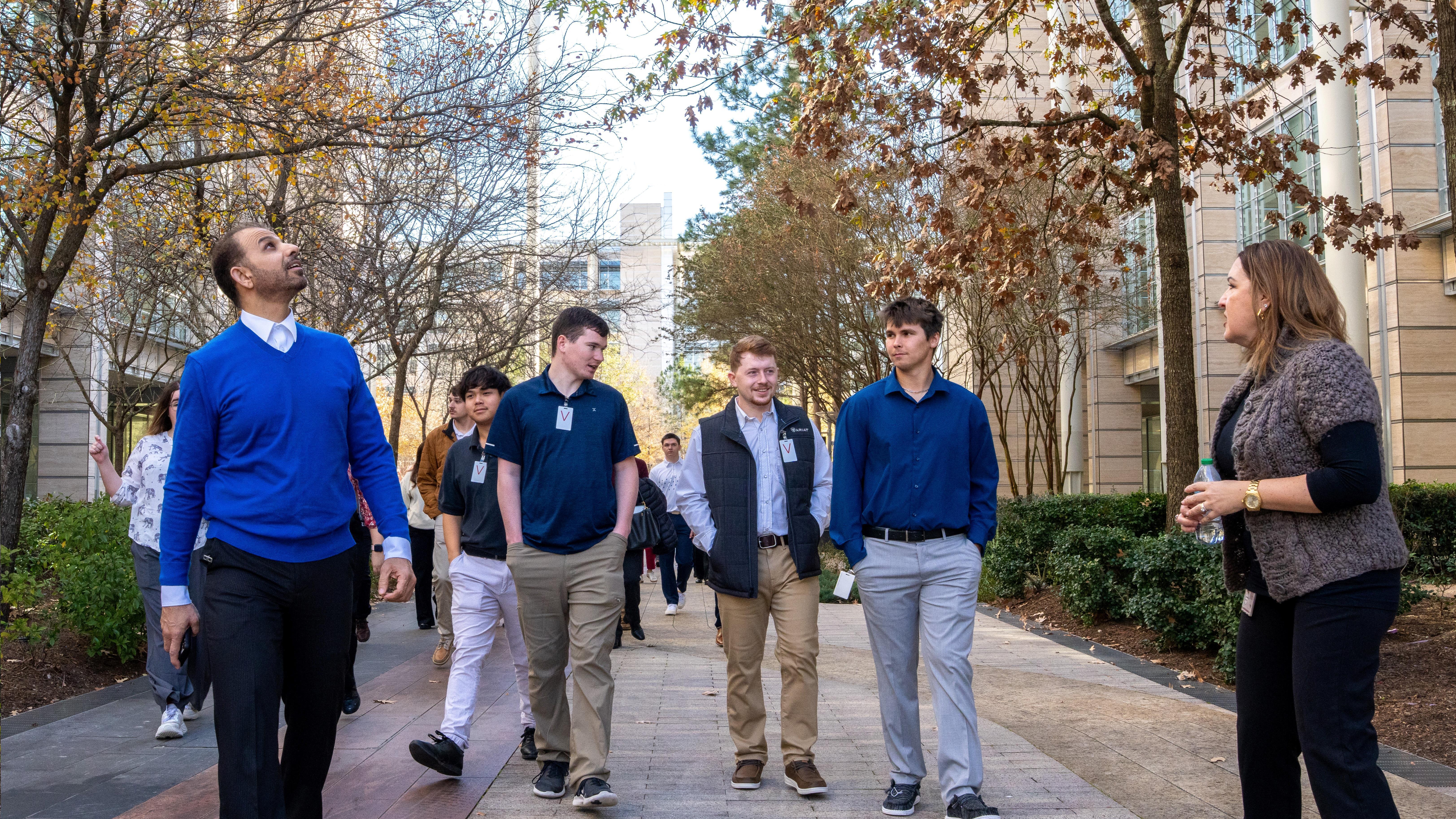A group of people walking outside on a paved path lined with trees and buildings during autumn.