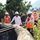 A group of people wearing hard hats and orange safety vests are gathered outdoors.