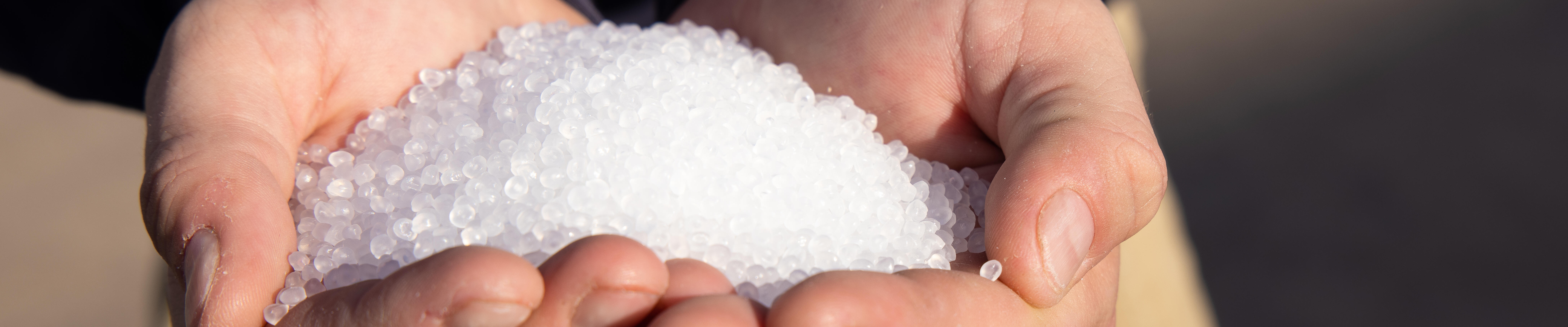 A person holding a handful of white plastic pellets.