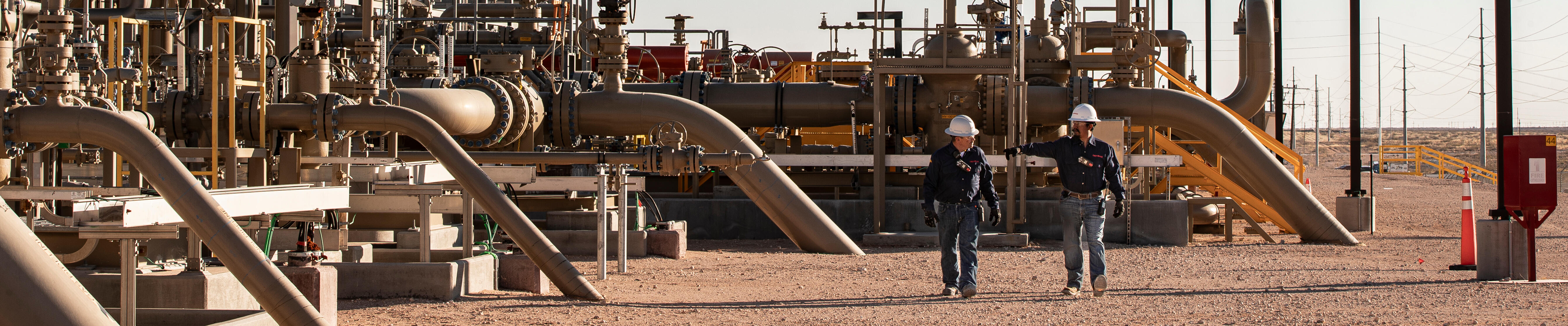 two people walking through large pipes and pipelines at facility in arid area