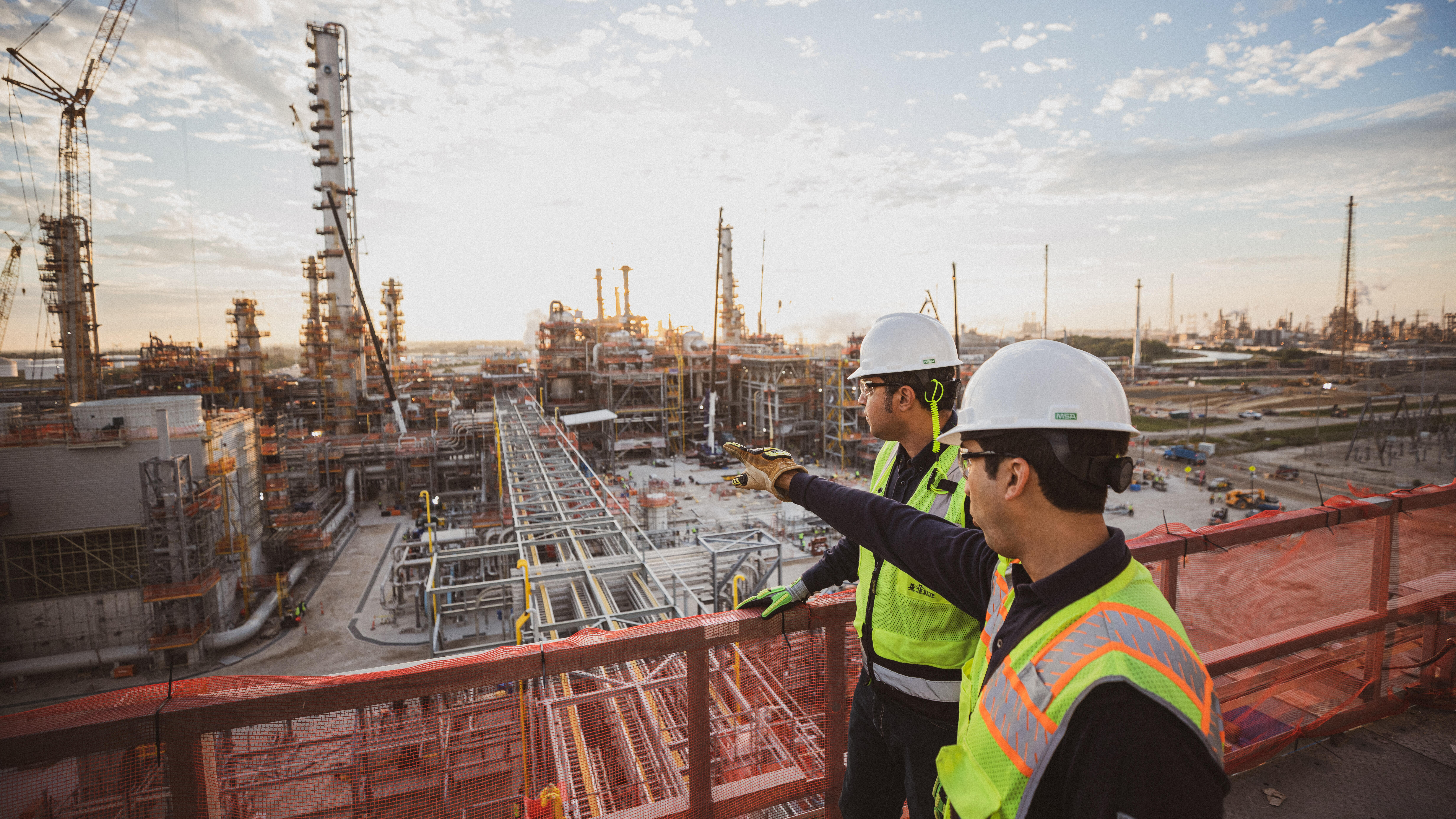 two workers standing on elevated platform overlooking construction at petrochemical facility