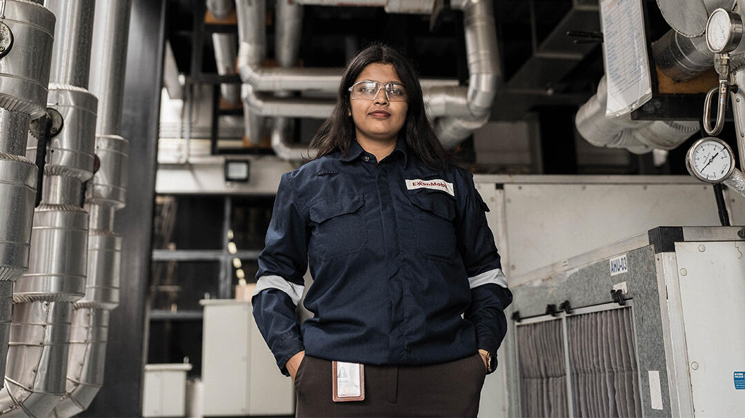female ExxonMobil employee standing in front of pipes, ducts and electrical boxes