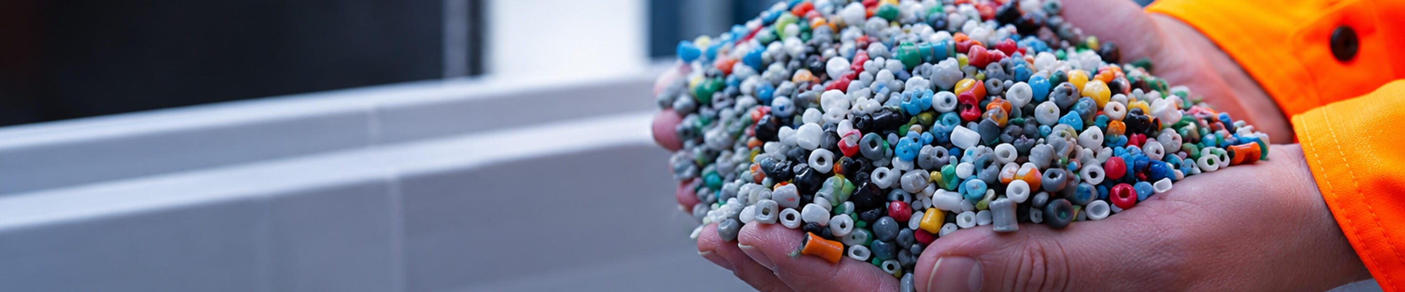 A person wearing an orange sleeve holds a large handful of small, multicolored plastic pellets or beads.