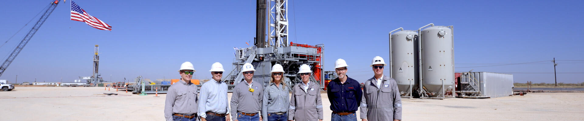 Group of ExxonMobil employees standing near a drilling rig.