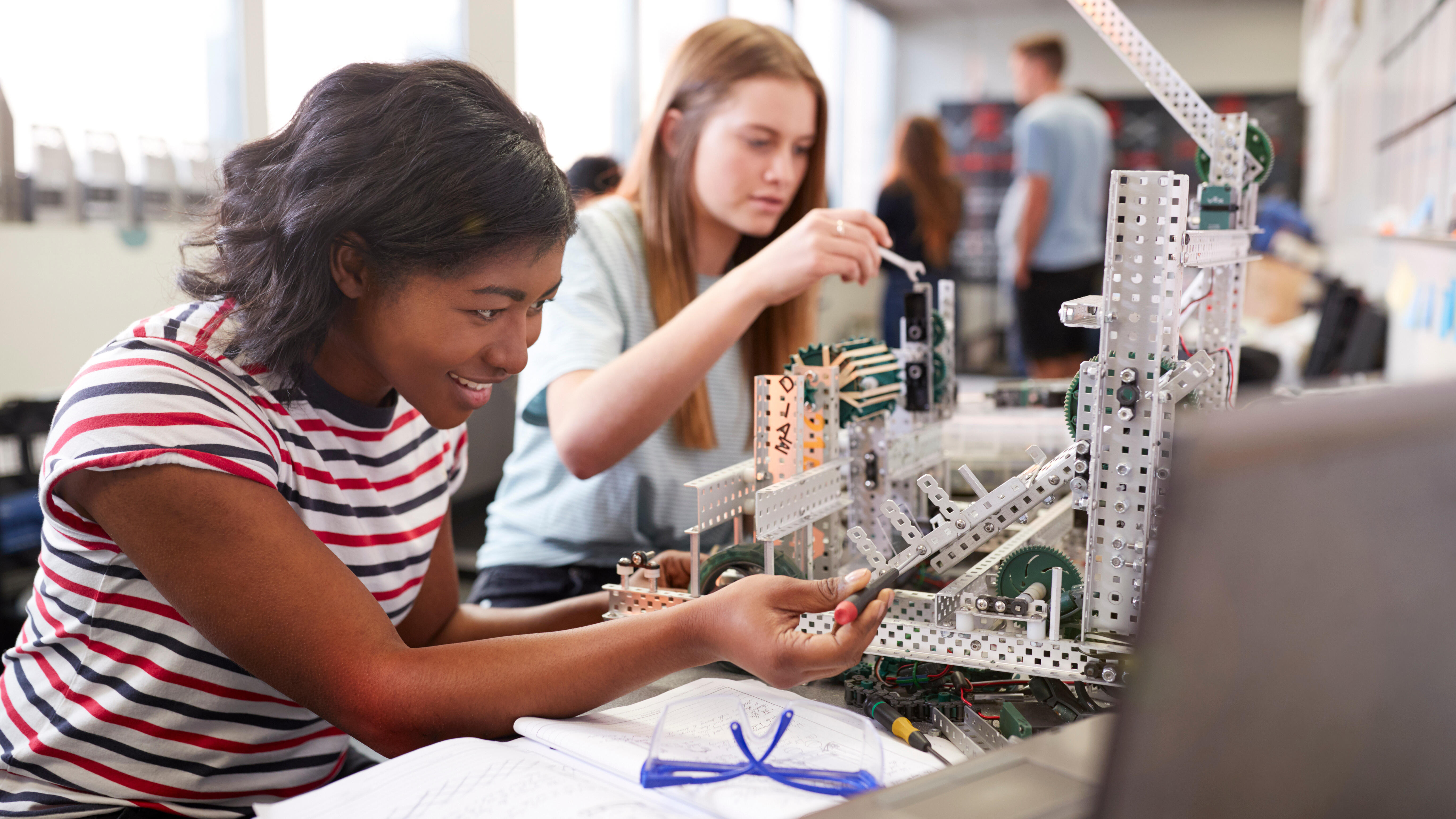 Two students are working together on assembling a robotics project using metal structural components, gears, and various mechanical parts.