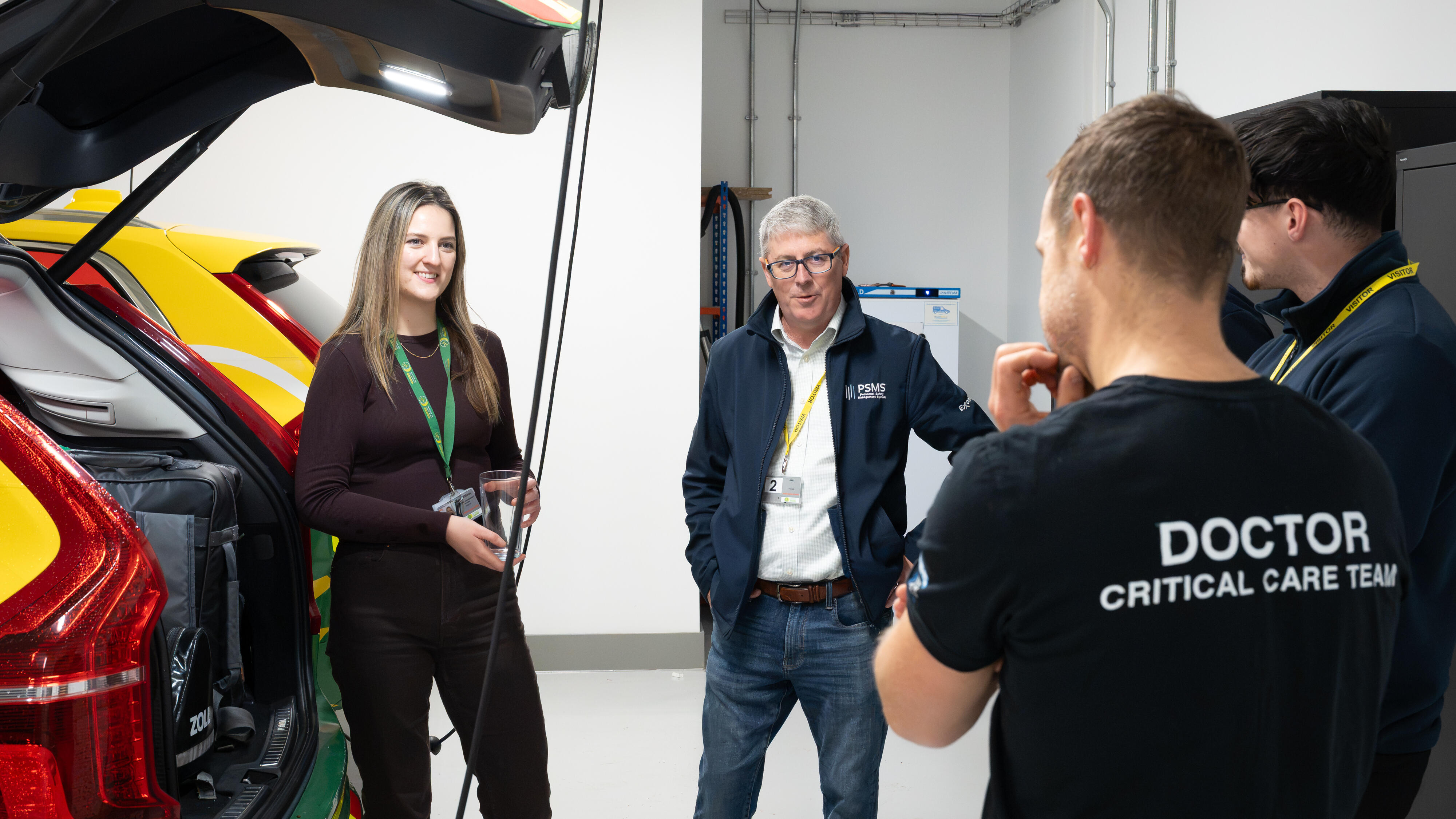 Four people stand beside an air ambulance response vehicle, viewing equipment and discussing emergency operations inside a facility.