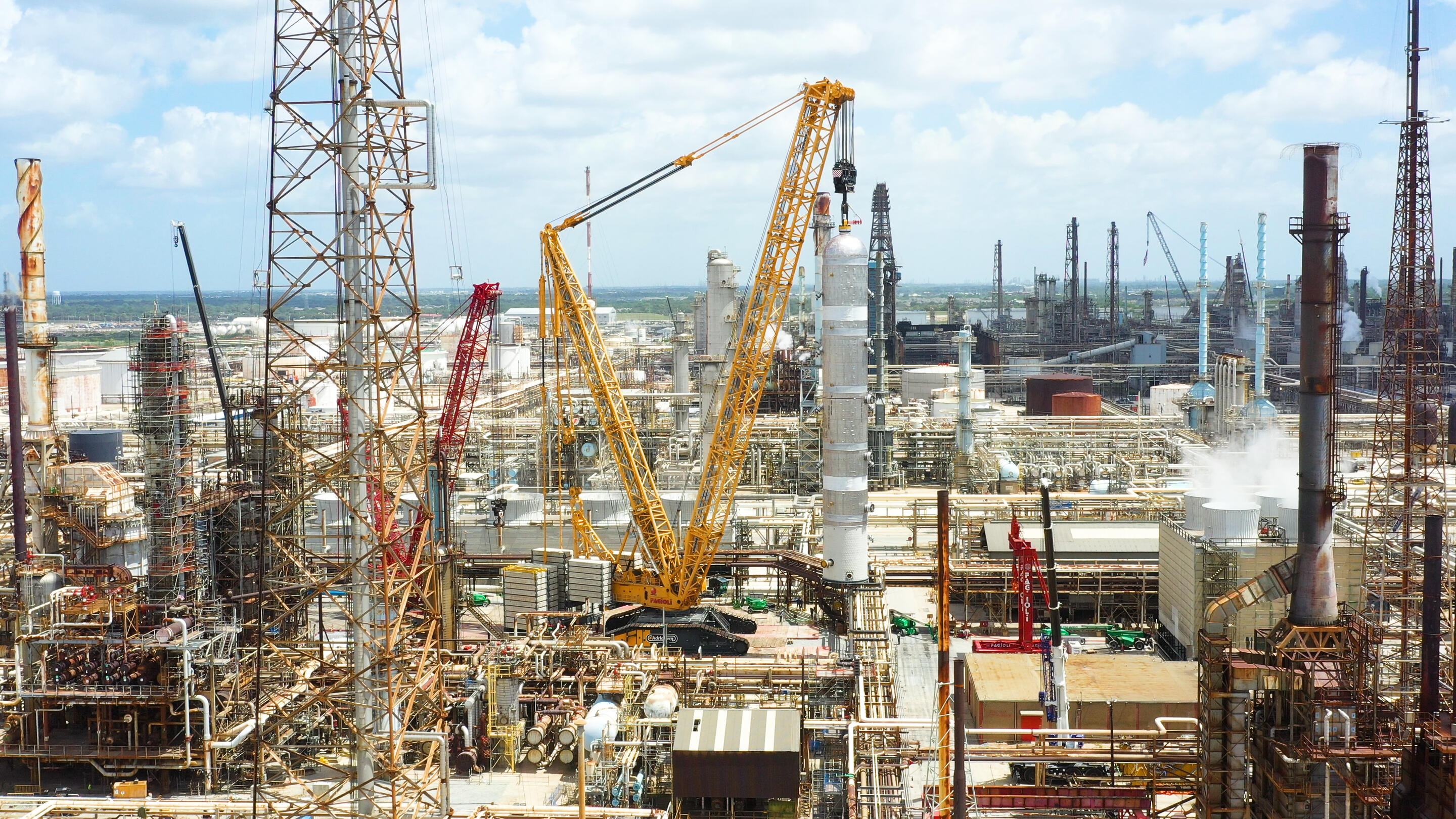 Industrial refinery complex stretches across the scene under a partly cloudy sky.