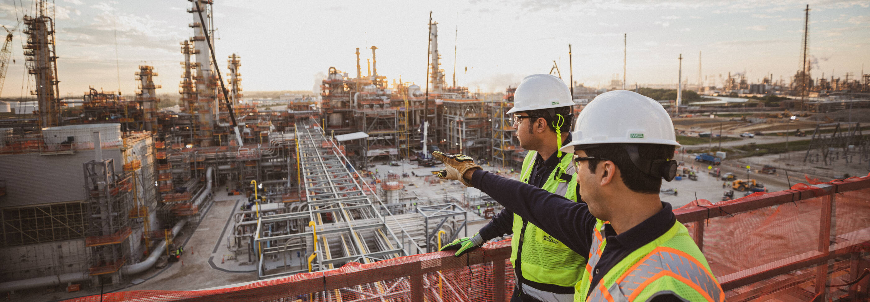 Image of two workers in vests and hard hats looking out at Baytown refinery.