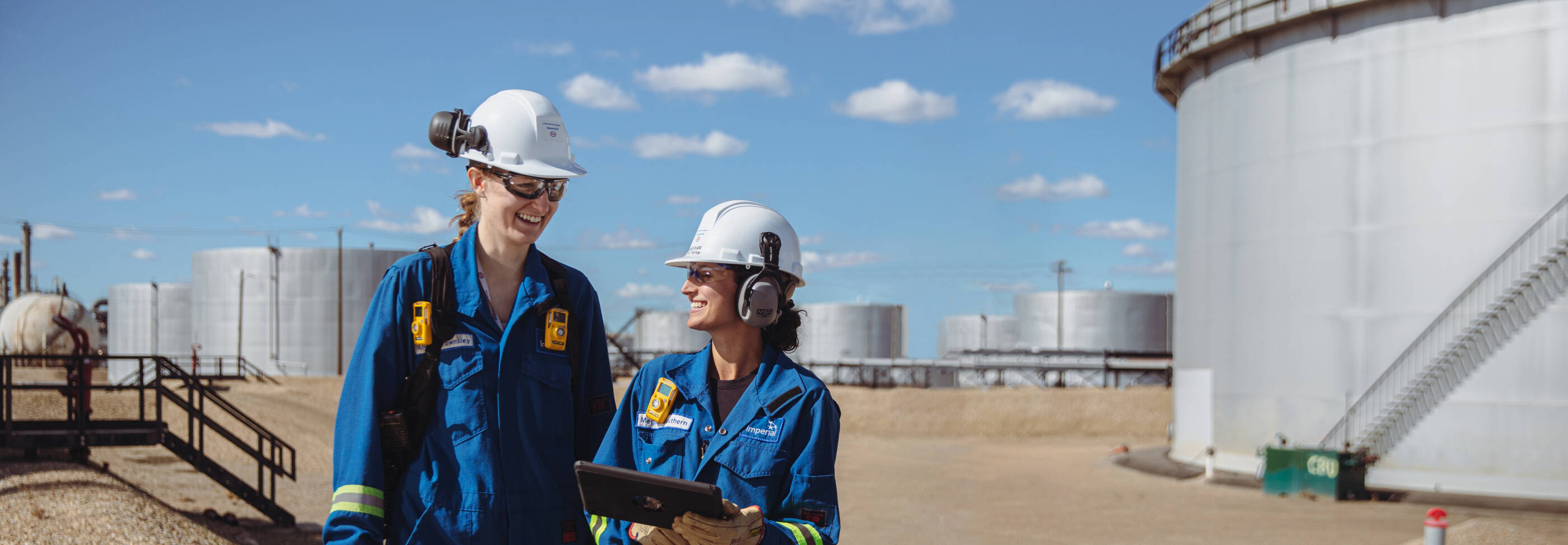 female refinery workers in front of white tanks