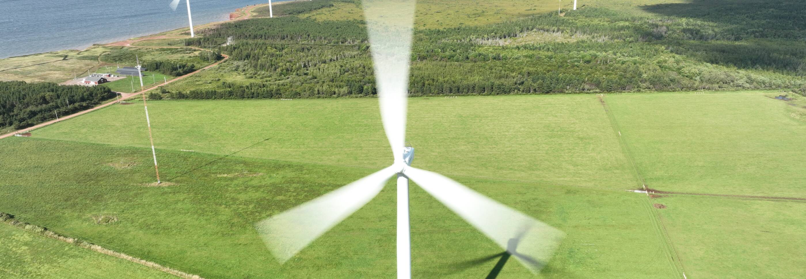 Wind farm over grassy fields next to a body of water.