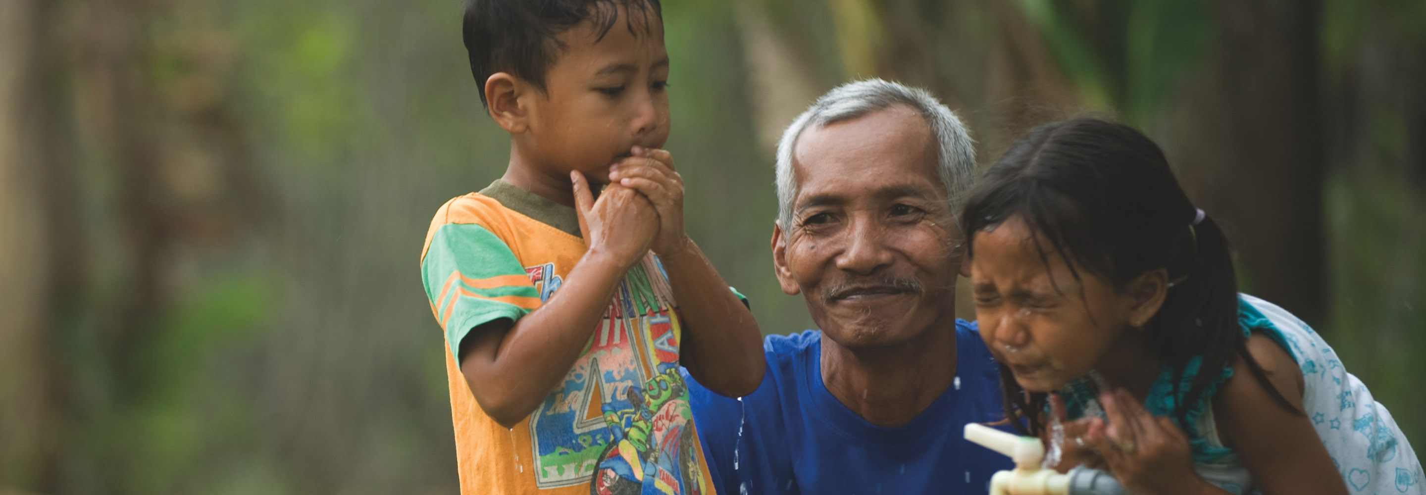 An elderly man with two children getting water from a spout