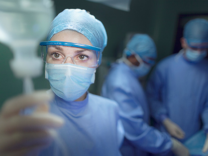 A doctor examines an IV drip in the operating room with two doctors in the background.
