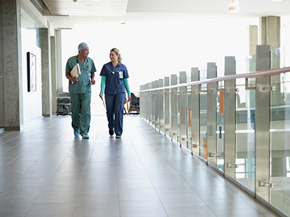 A male and female doctor walk down a hospital corridor.