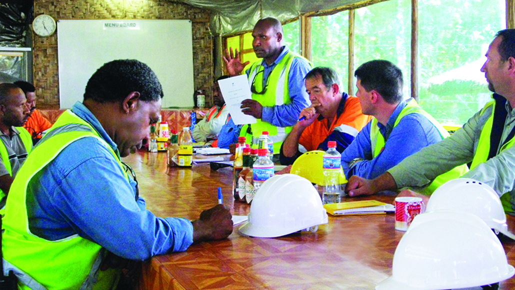 Workers in neon vests gathered around a table for a meeting