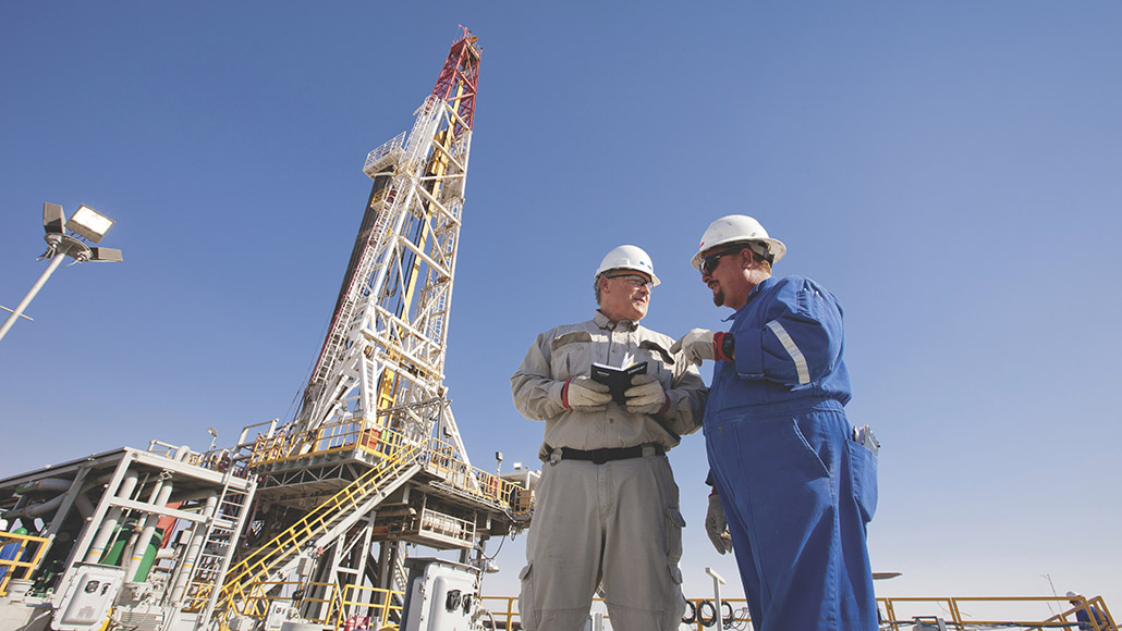 Two ExxonMobil employees wearing white hard hats and blue and grey uniforms at an oil rig