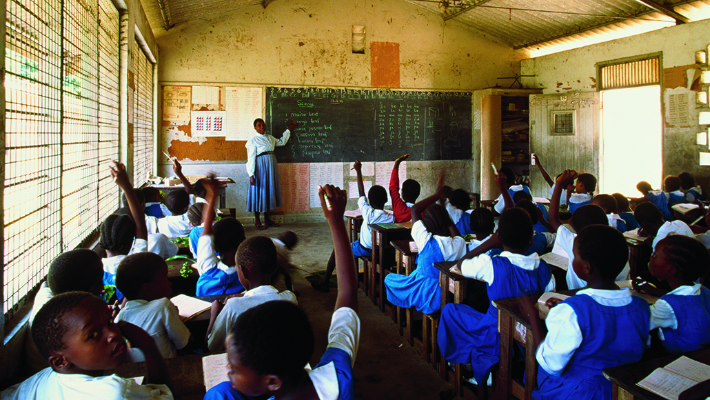 Teacher in classroom pointing to blackboard, Kenya