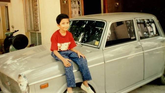 Young boy sitting on the hood of an old car