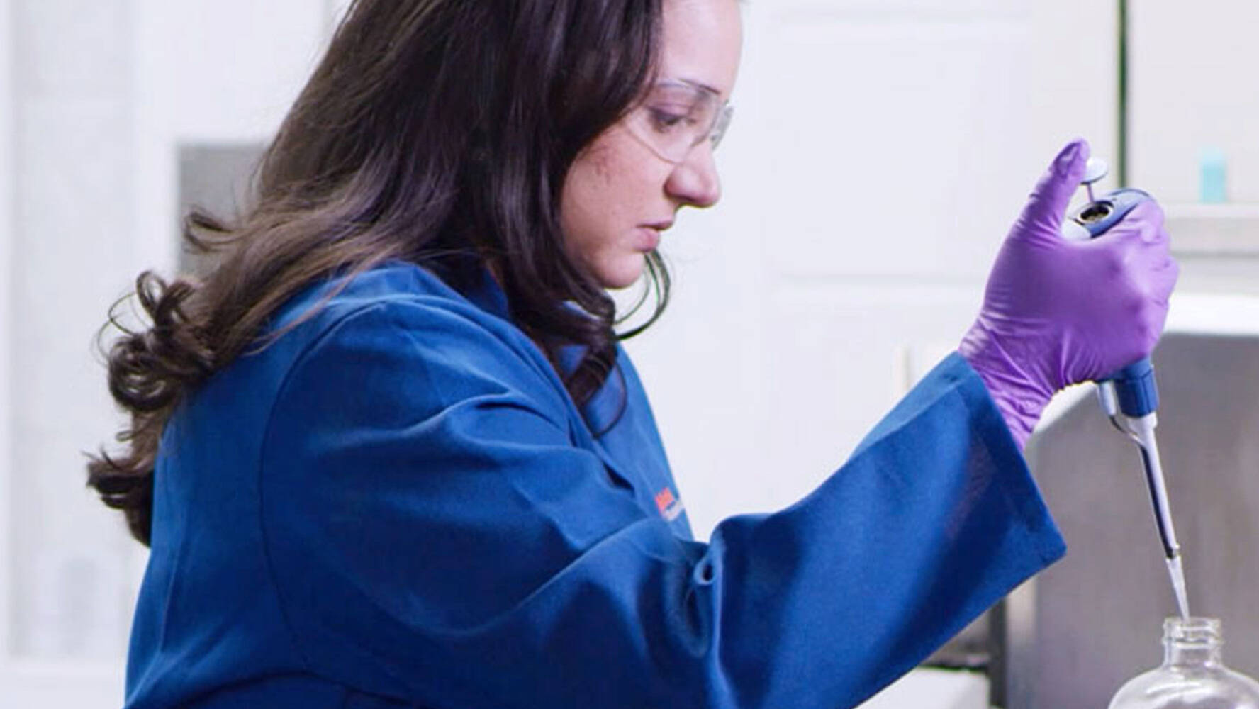 Scientist with blue lab coat and purple gloves in lab