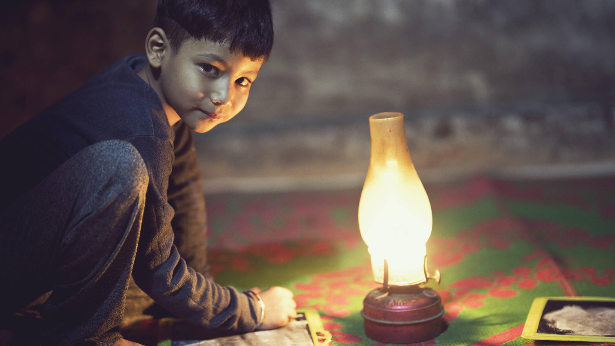 young boy with chalkboard illuminated by oil lamp